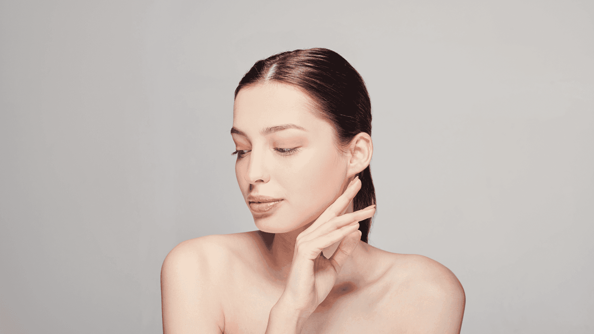 Woman with smooth skin and closed eyes gently touching her neck, facing sideways.