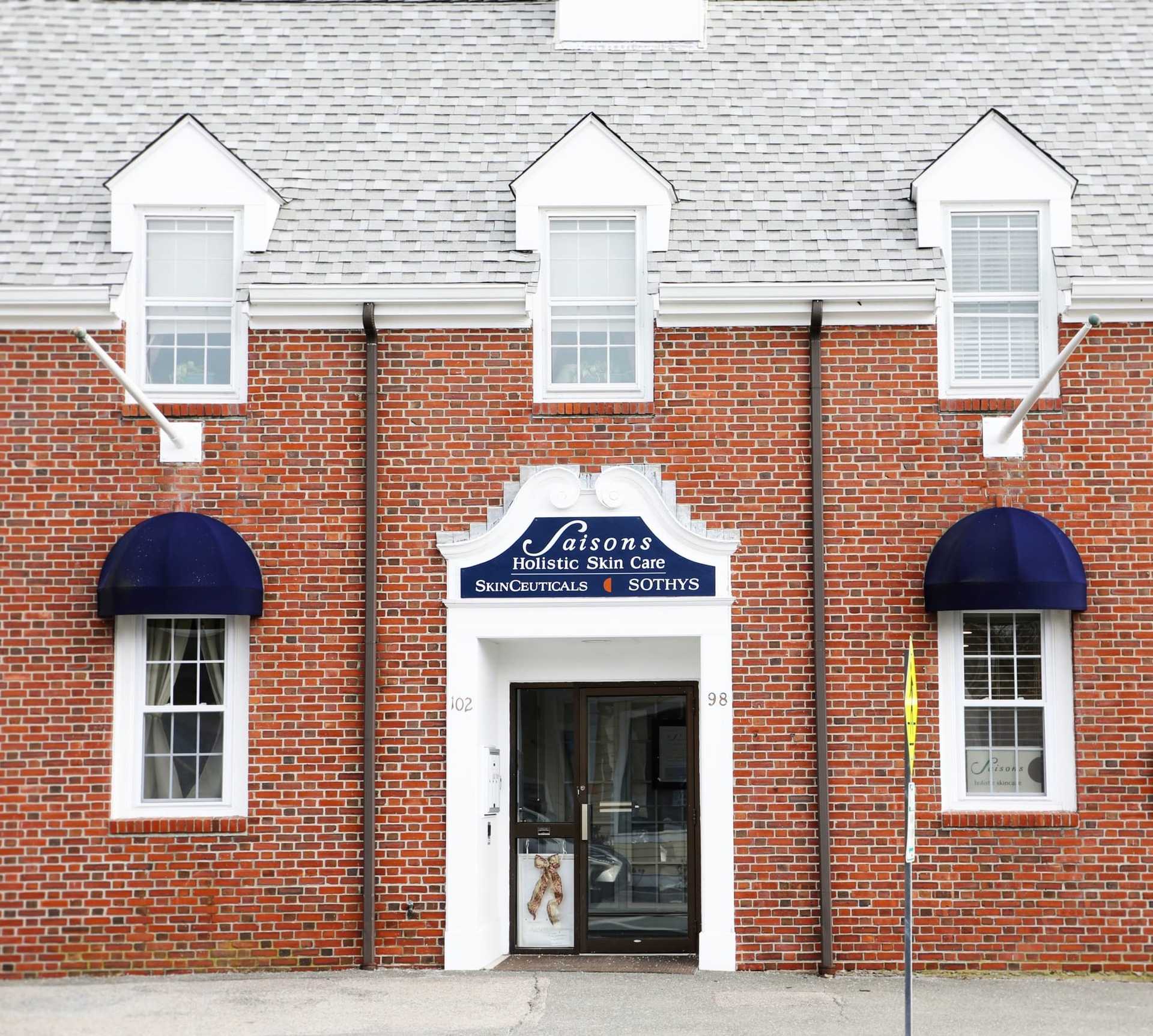 Brick building with a skincare clinic sign and blue awnings over windows and entrance.