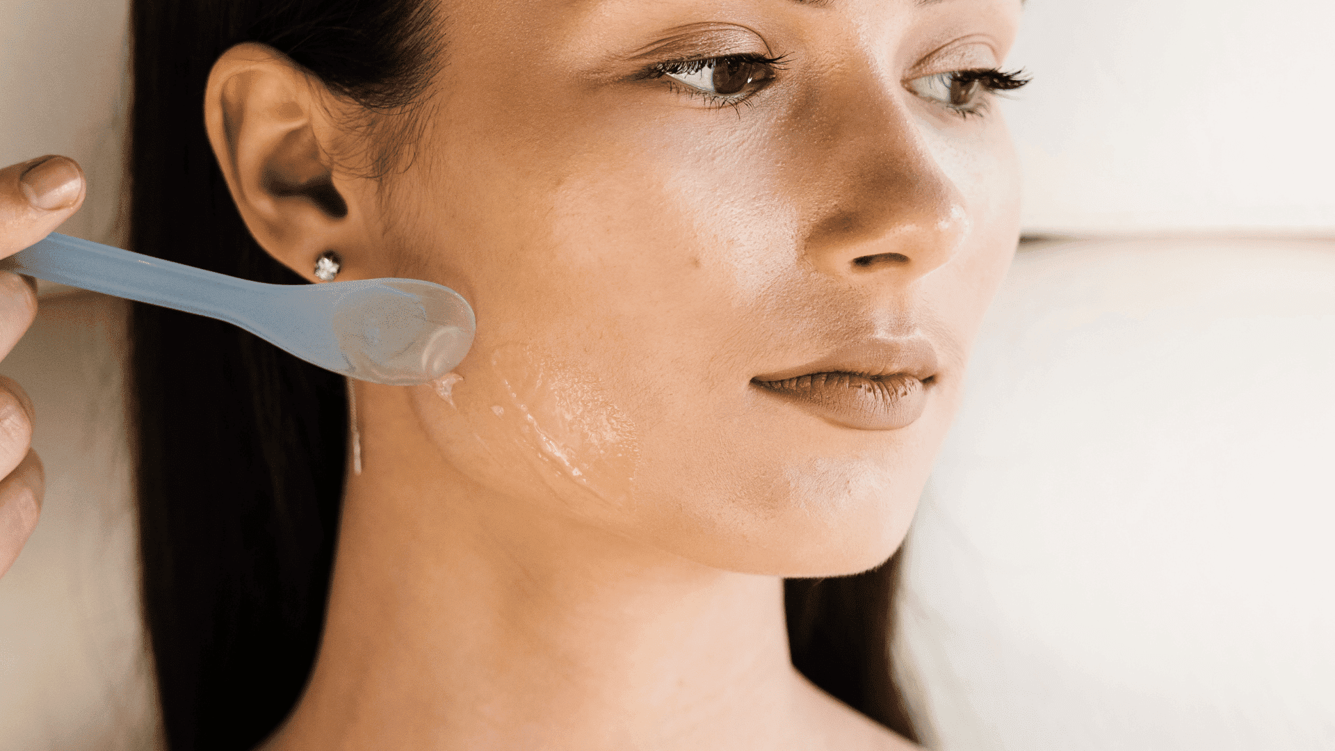 Person receiving a facial treatment with a plastic spoon applying gel to their cheek.