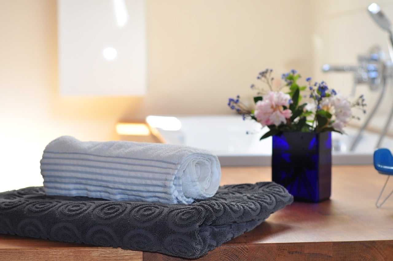 Folded towels and a blue vase with flowers on a wooden countertop in a bathroom setting.