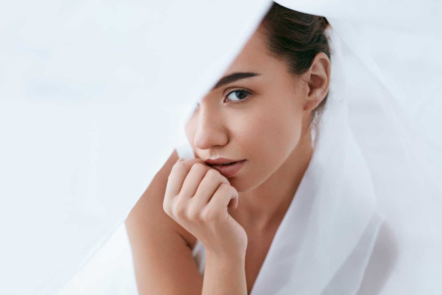 Close-up of a woman with a thoughtful expression, partially covered by a white veil.