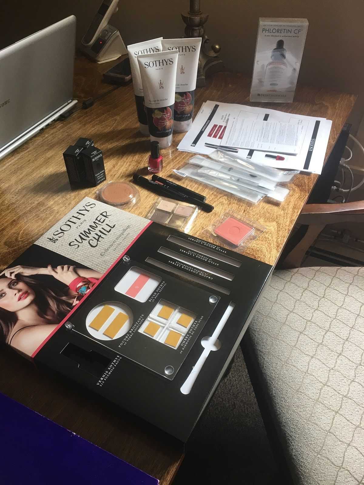Beauty products and makeup set displayed on a wooden desk with a chair and documents.