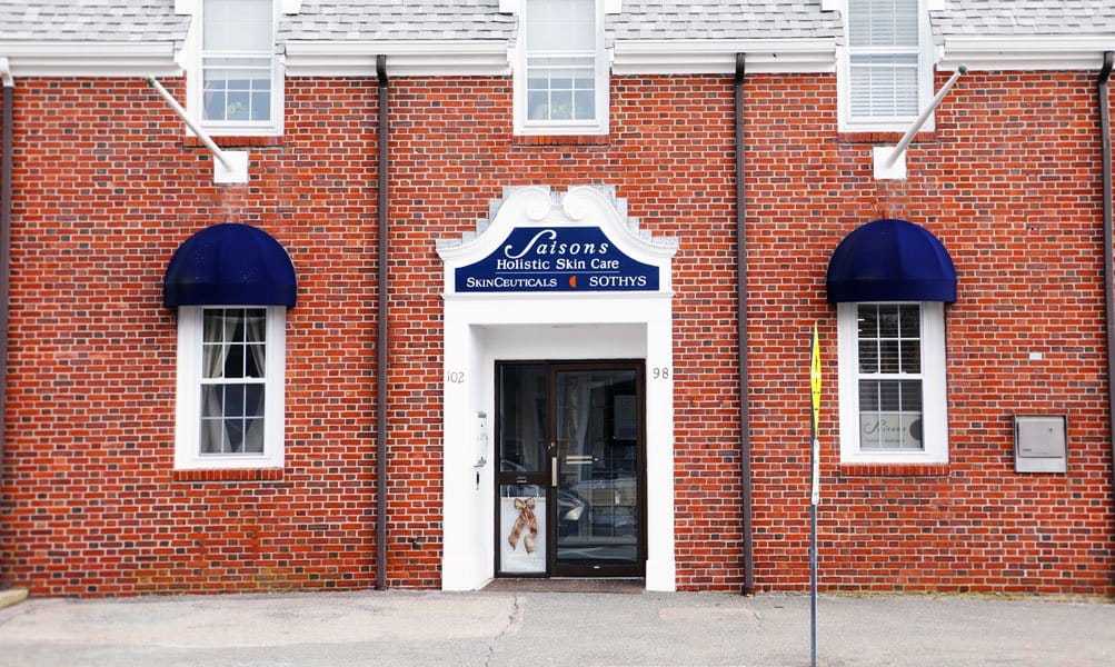 Saisons Holistic Skin Care storefront with red brick facade and blue awnings on windows.