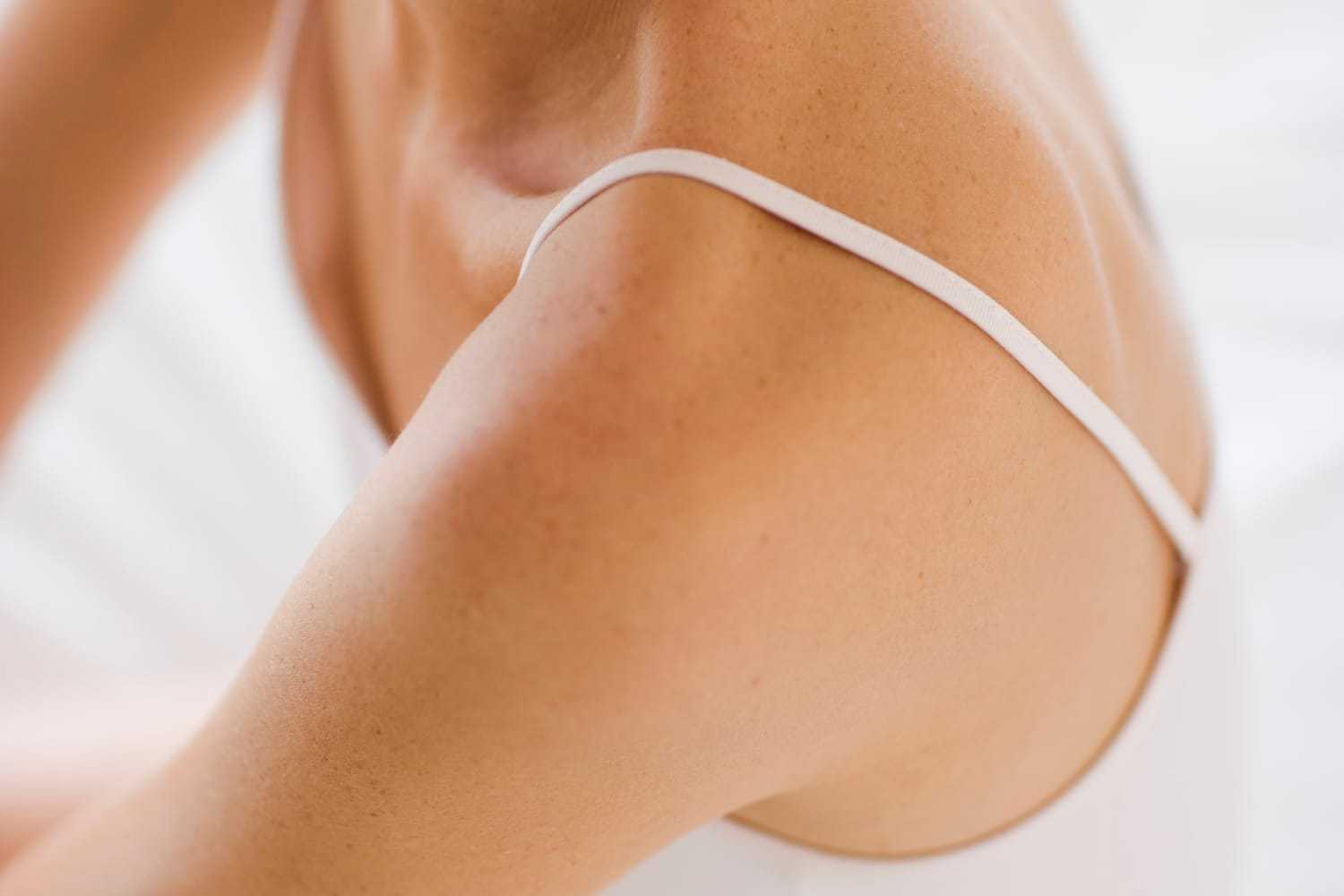 Close-up of a person's shoulder and upper arm wearing a white spaghetti strap top.