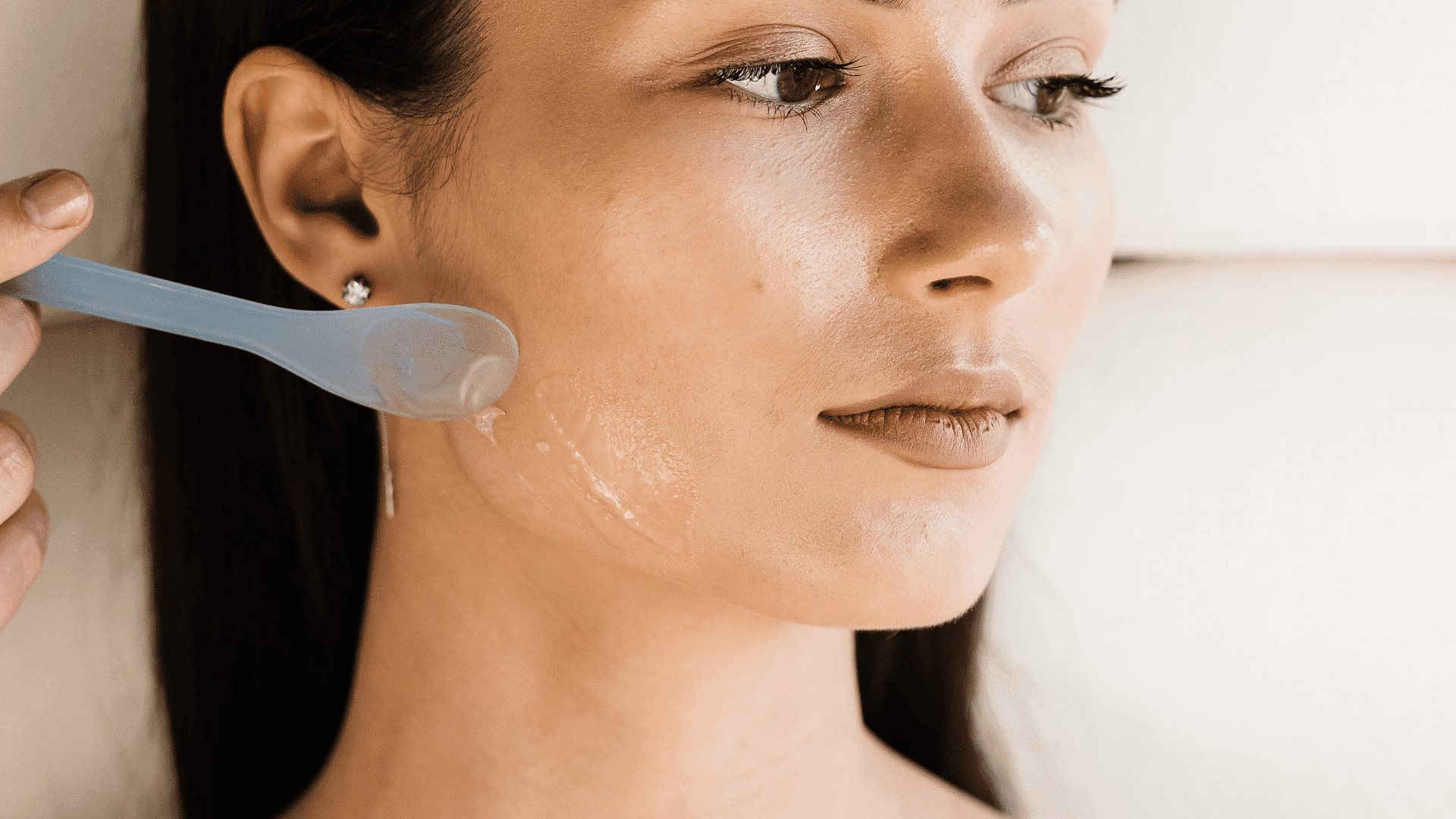 Person receiving a facial treatment with a plastic spoon applying gel to their cheek.