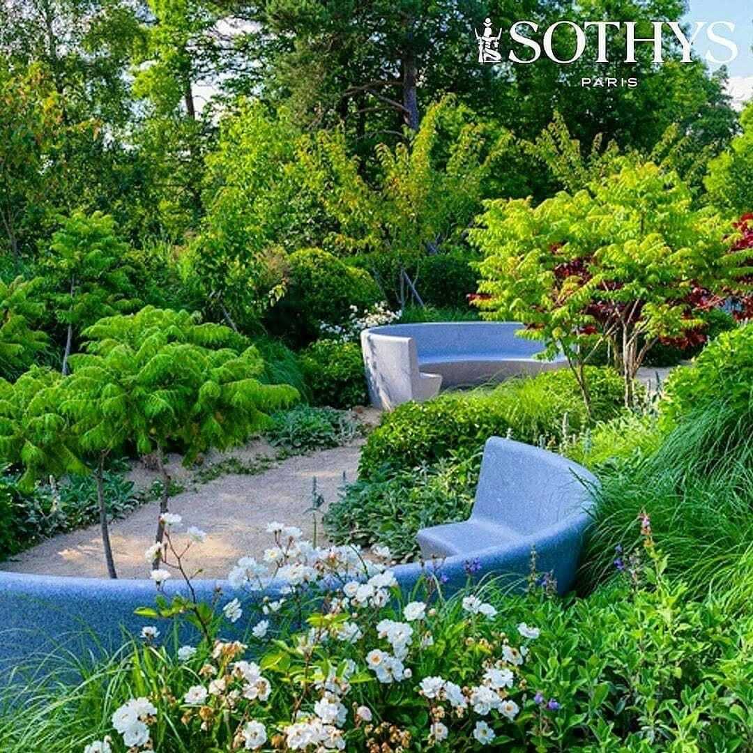 Lush garden with curved stone benches, vibrant greenery, and colorful flowers.
