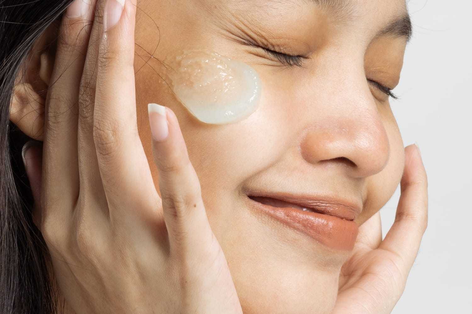 Woman applying skincare product to her cheek with a content expression.