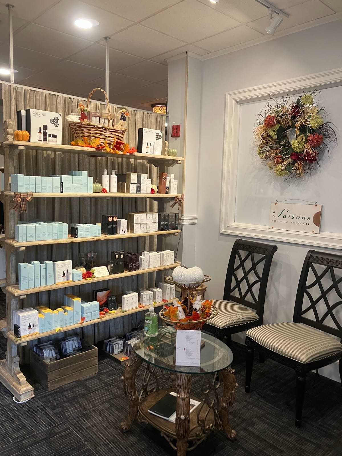 Cozy boutique with shelves of beauty products, fall decor, and two chairs near a table.